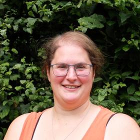 Die Küsterin Mareike Wellmann steht vor einer grünen Hecke