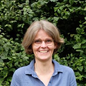 Die Pastorin Kerstin Keßler steht vor einer grünen Hecke